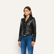 A model wears a Blakely Embroidered Leather Jacket, an embroidered lambskin biker jacket featuring small red hearts and black spade symbols, paired with blue jeans.