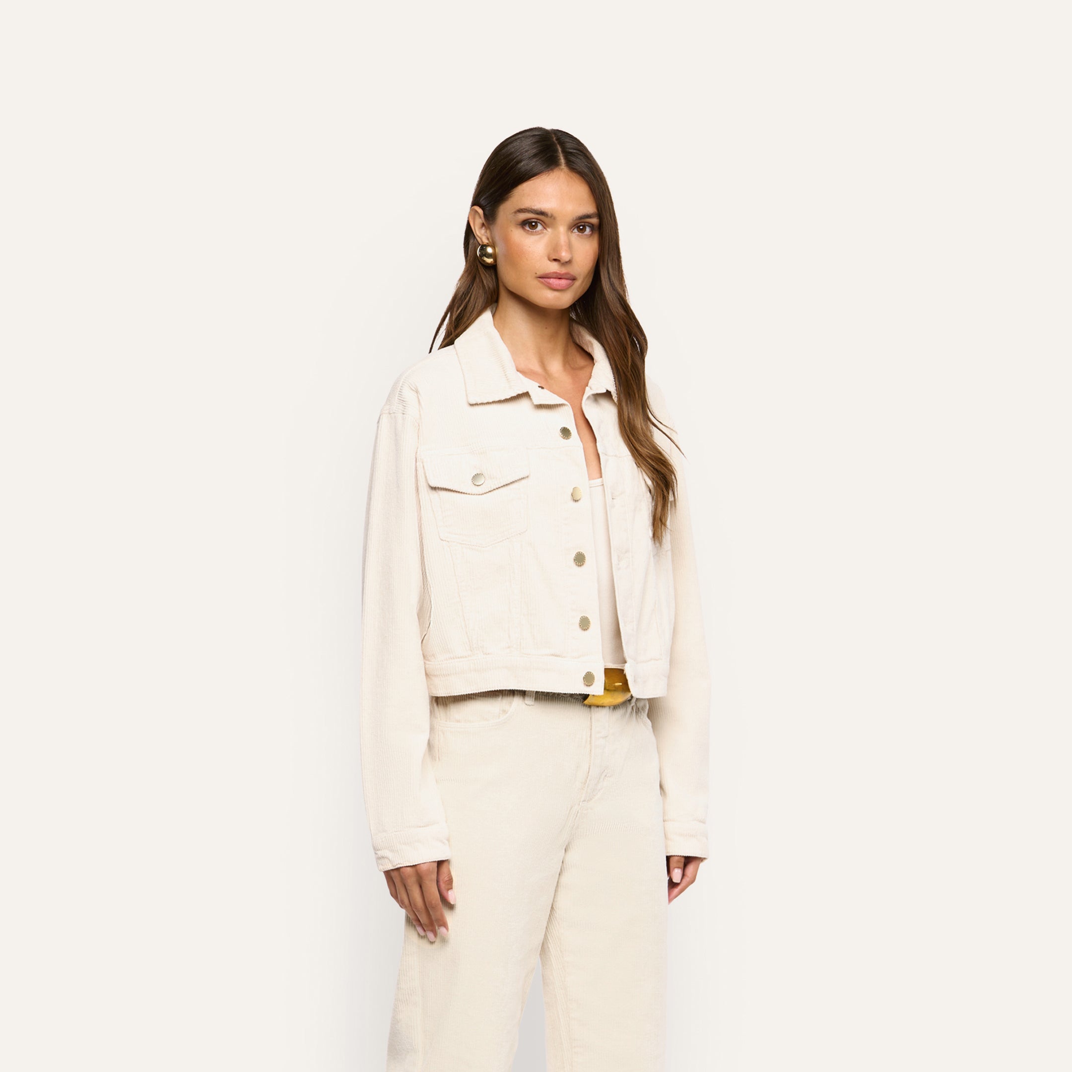 A woman wearing an Alessia Corduroy Jacket in pearl white, featuring a cropped fit and metal buttons.