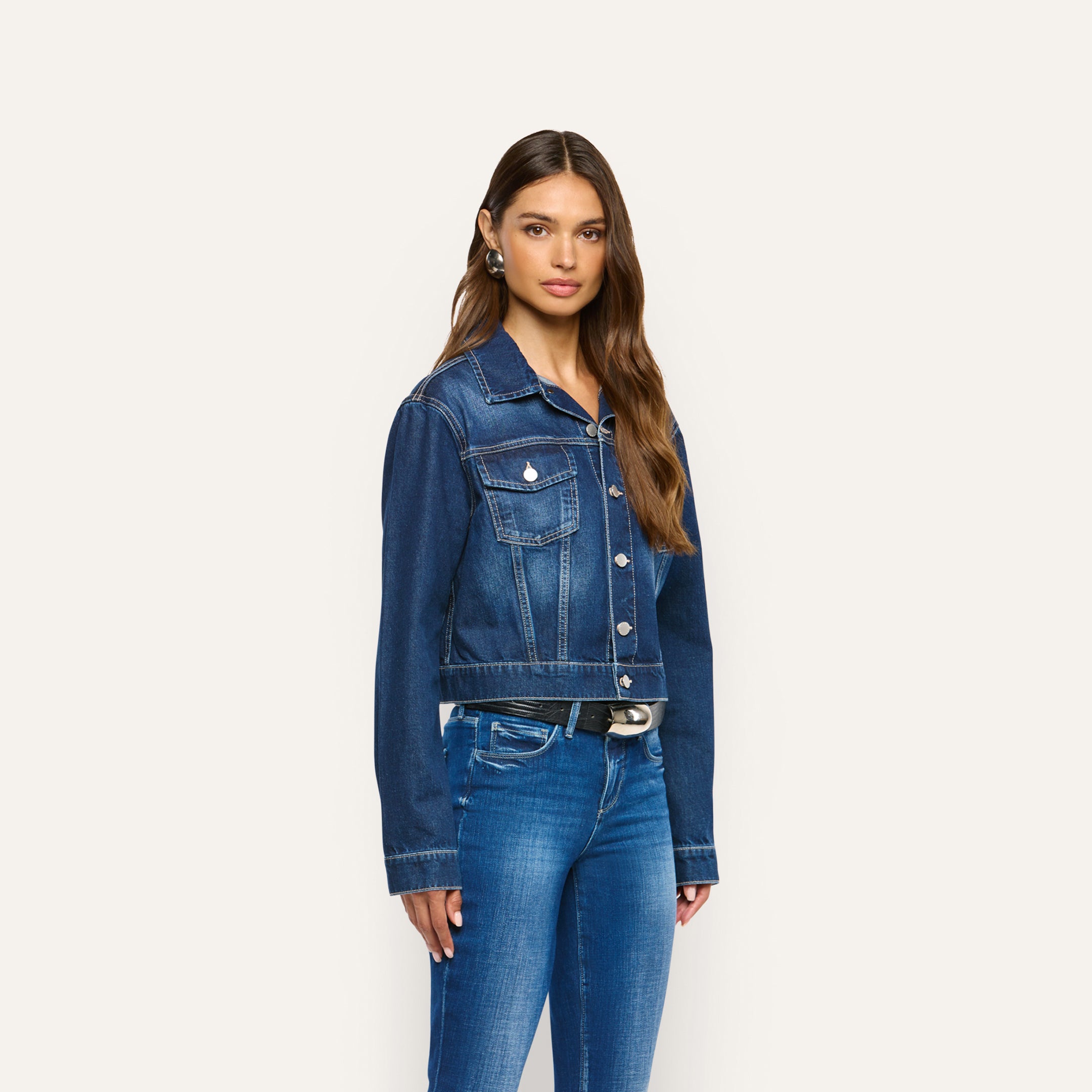 A person wearing a cropped dark-wash Alessia Jean Jacket featuring a button-front closure and two chest pockets.