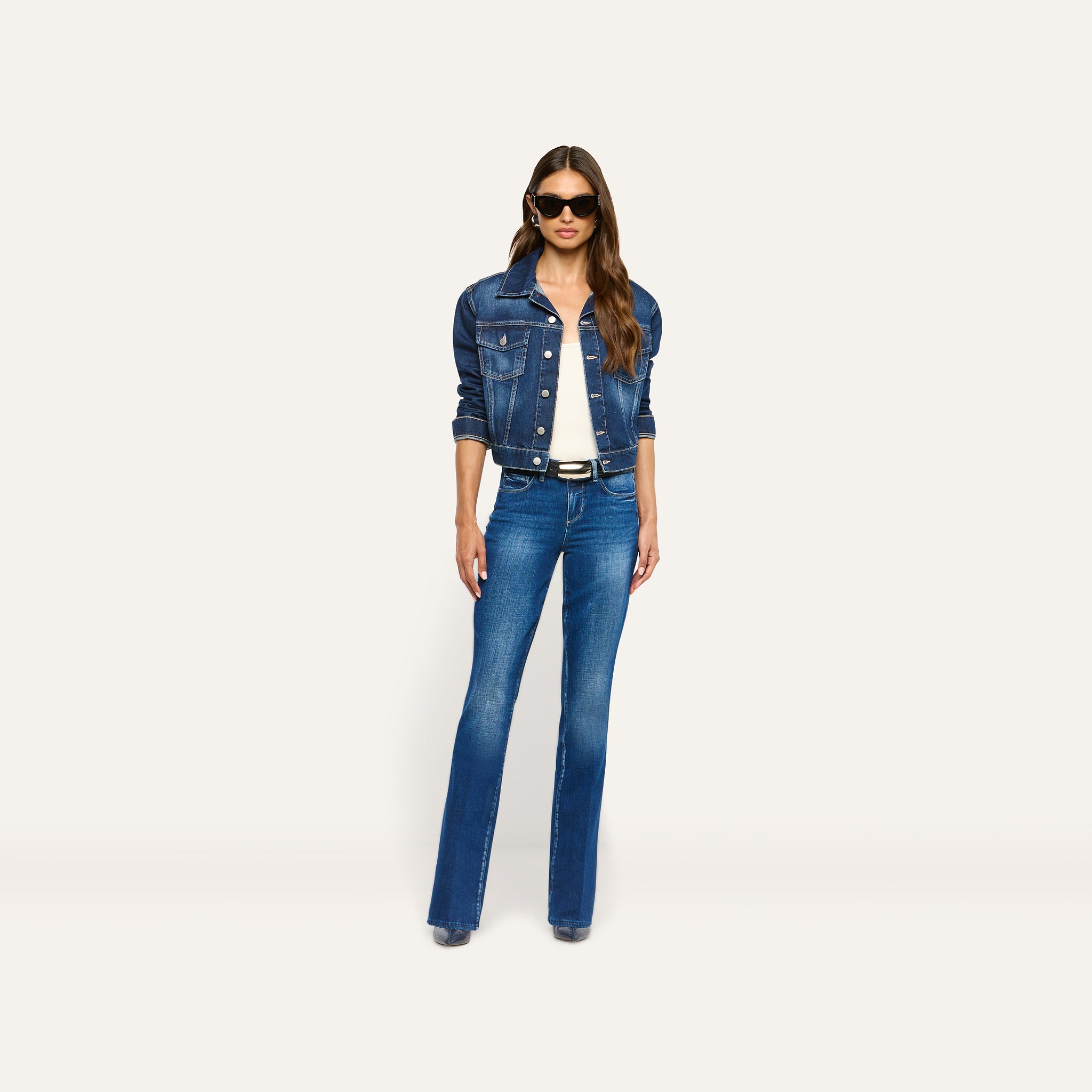 Alessia wears an Alessia Jean Jacket in dark wash over a white top, paired with blue flare jeans, a black belt, and sunglasses.