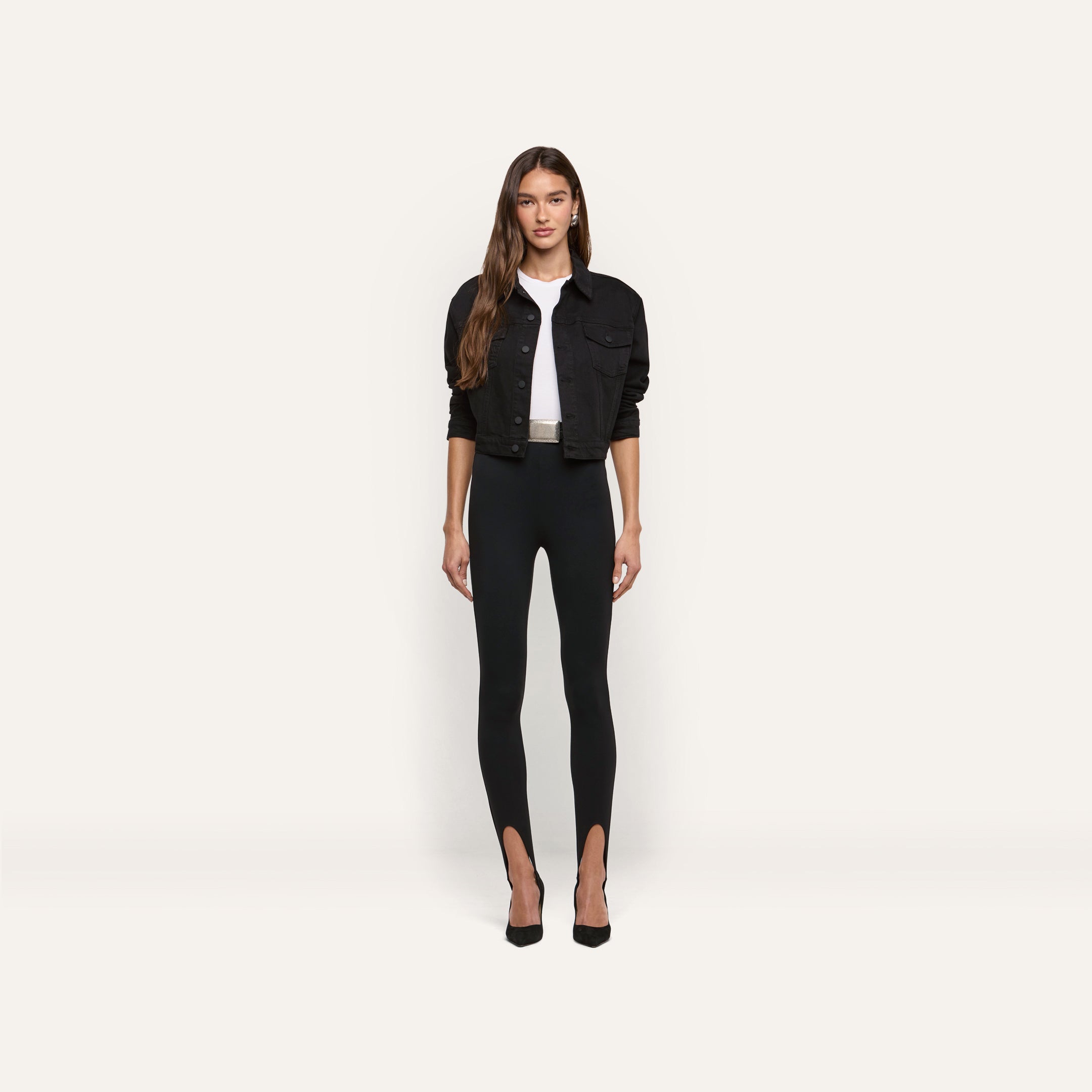 A person wears a cropped black Alessia Jean Jacket over a white t-shirt and black stirrup leggings, paired with black high-heeled pumps.