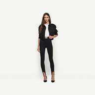 A person wearing a black Alessia Jean Jacket over a white t-shirt, black stirrup leggings with a belt, and black pointed-toe heels.