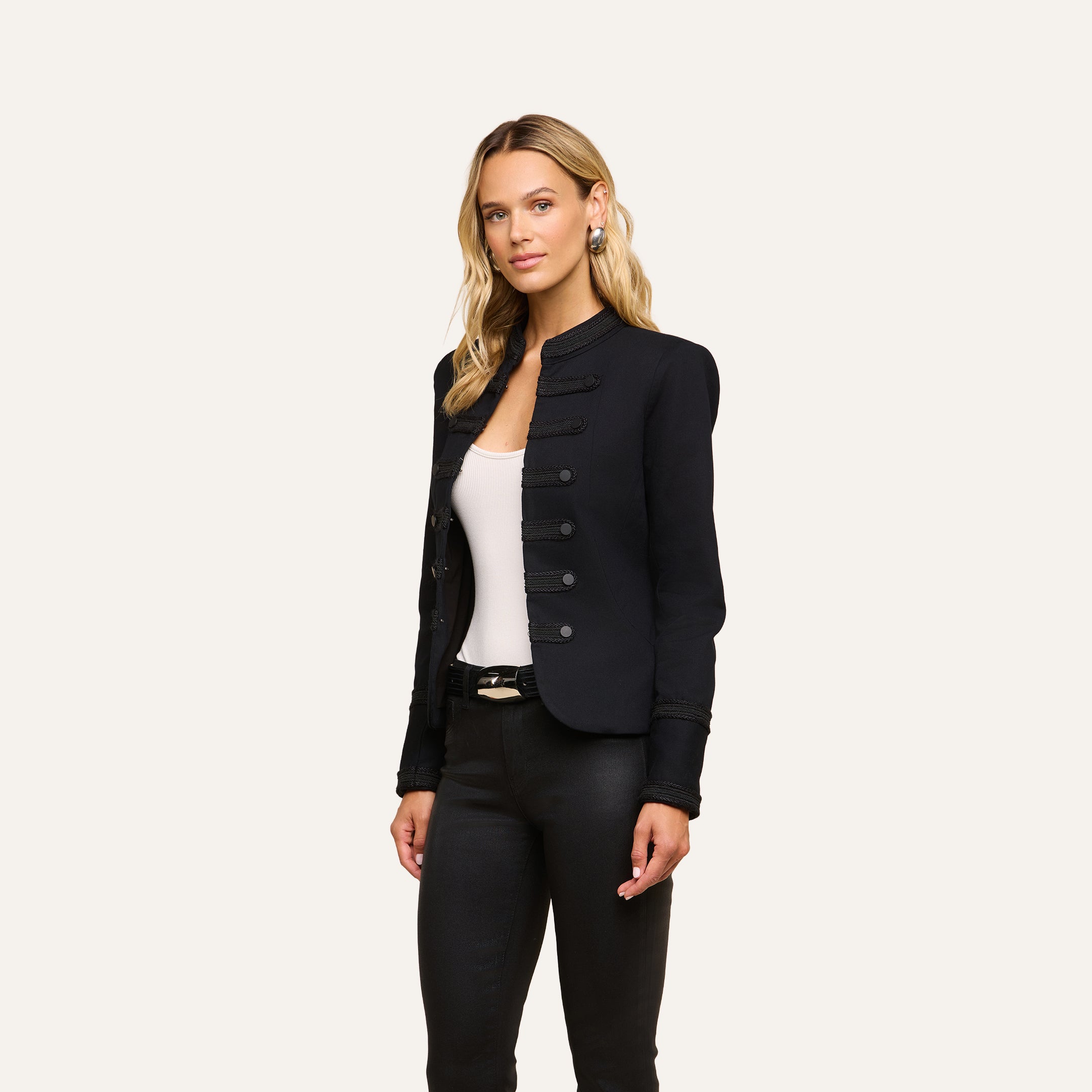 A woman with long blonde hair and minimal accessories stands against a plain background wearing the vintage-inspired Victory Jacket in black over a white top and black pants.