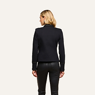 A woman with blonde hair, wearing the Victory Jacket and black leather pants, stands with her back to the camera against a plain light background.