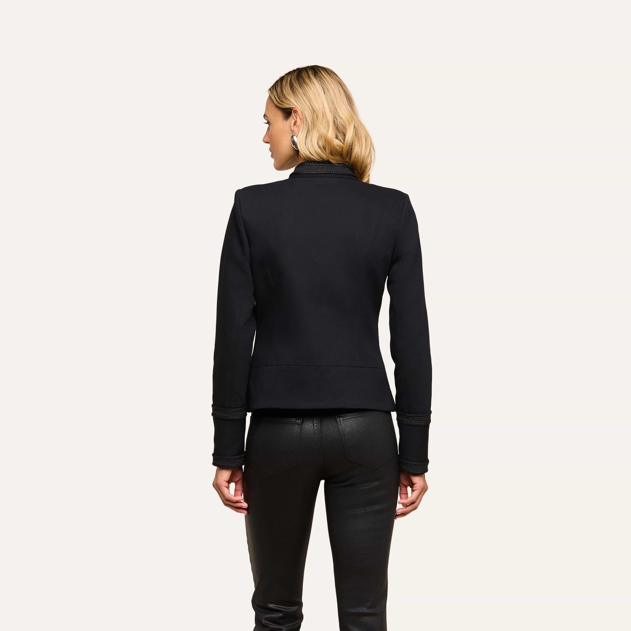 A woman with blonde hair, wearing the Victory Jacket and black leather pants, stands with her back to the camera against a plain light background.