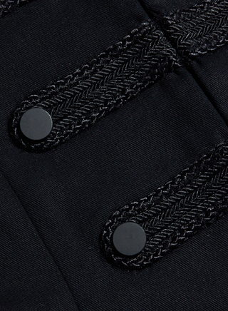Close-up of a black fabric with two round black buttons and decorative braided trim running horizontally across the material.