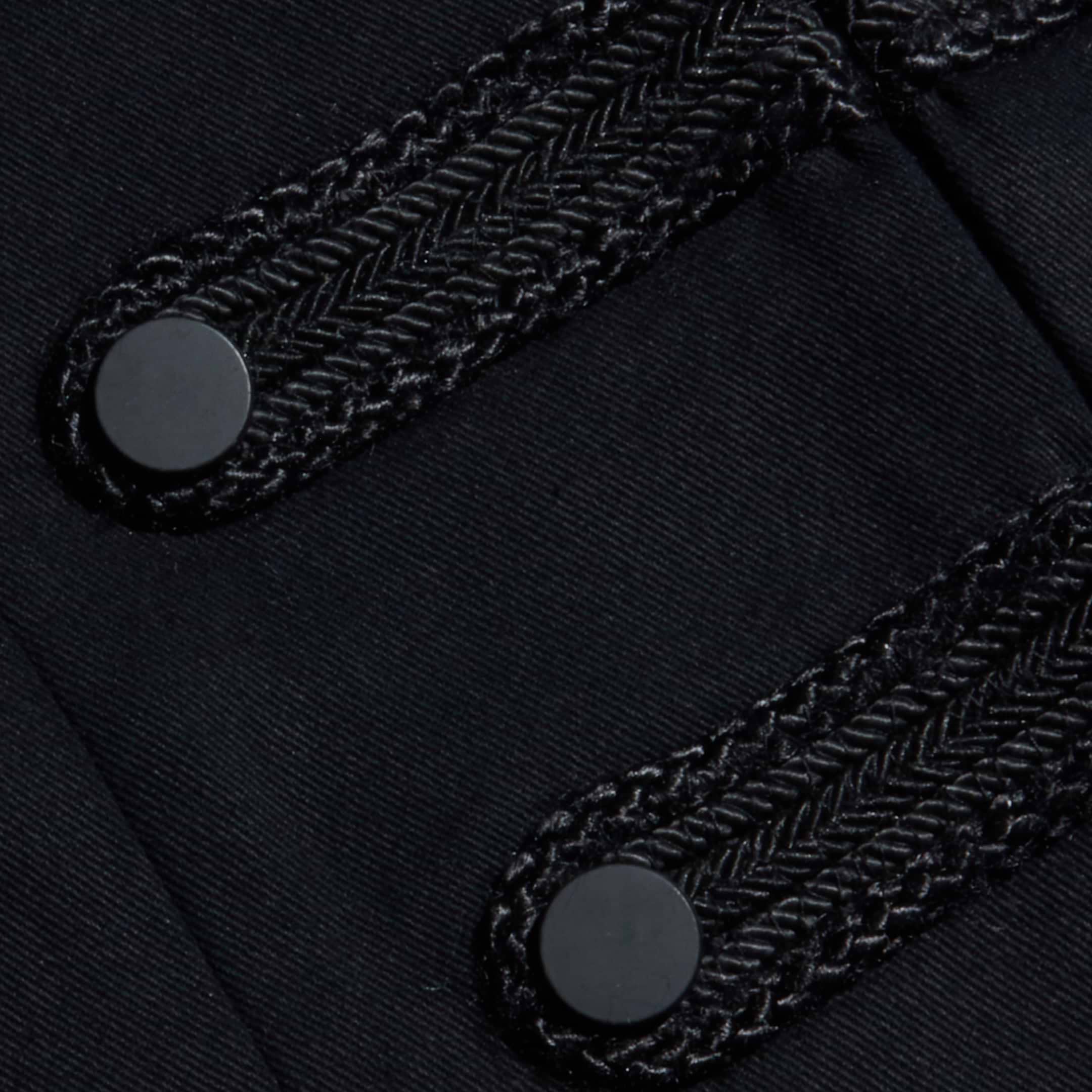 Close-up of two black, braided decorative bands with round black buttons on a dark fabric, detailing the Victory Jacket.