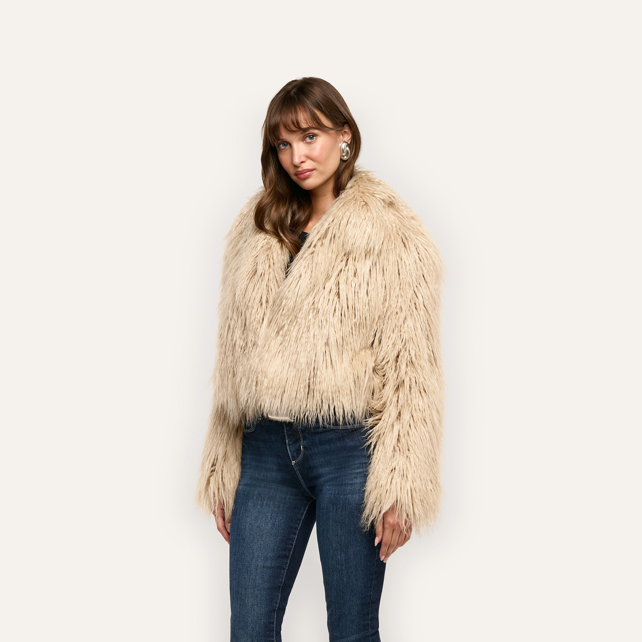 A person wearing a beige, cropped shag Fenella Faux Fur Coat and blue jeans.