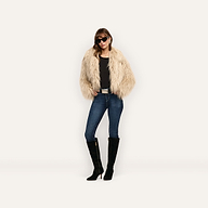 A person wears a cropped, shaggy beige Fenella Faux Fur Coat over a black top, blue jeans, and black knee-high boots, accessorized with sunglasses.