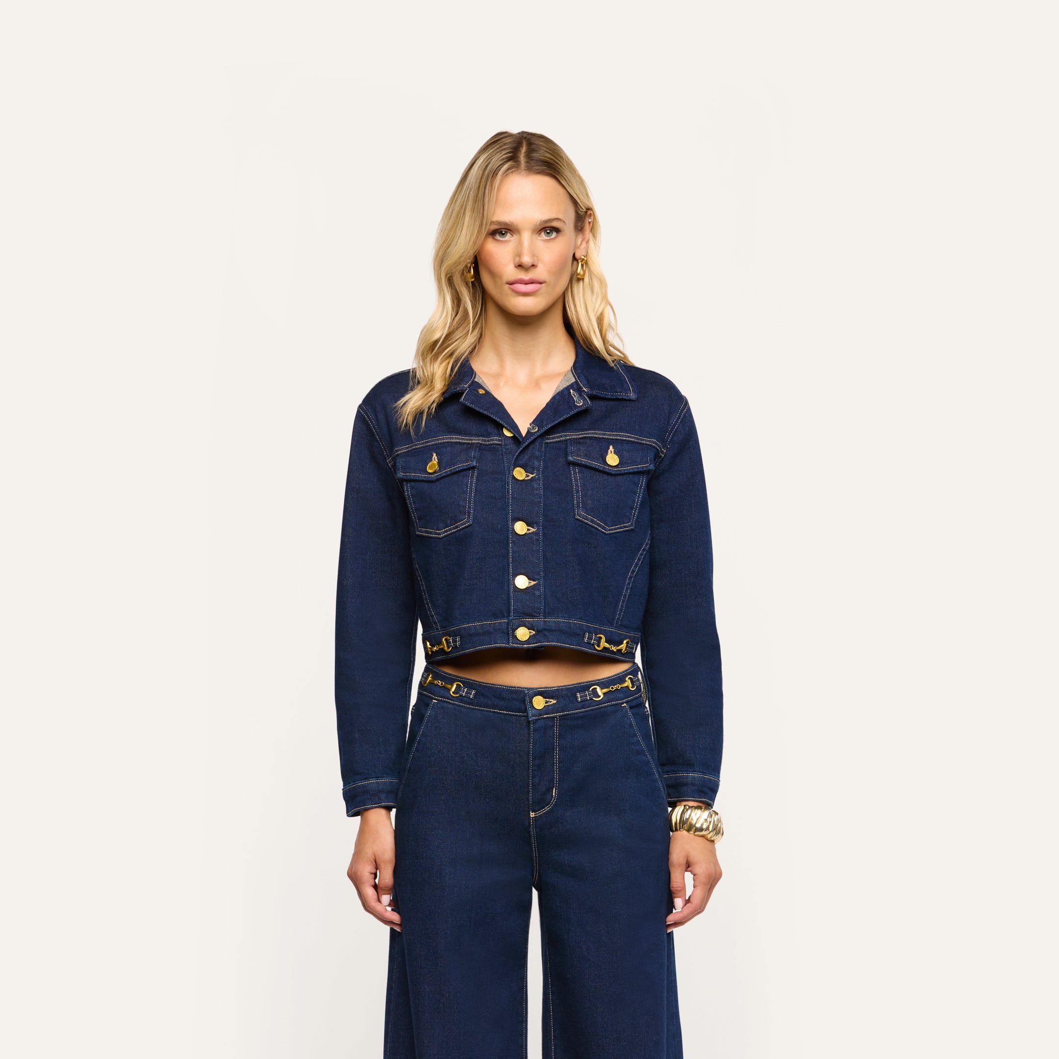 A person wearing an Edin Jean Jacket in cropped indigo wash denim with gold-tone buttons and matching wide-leg jeans.