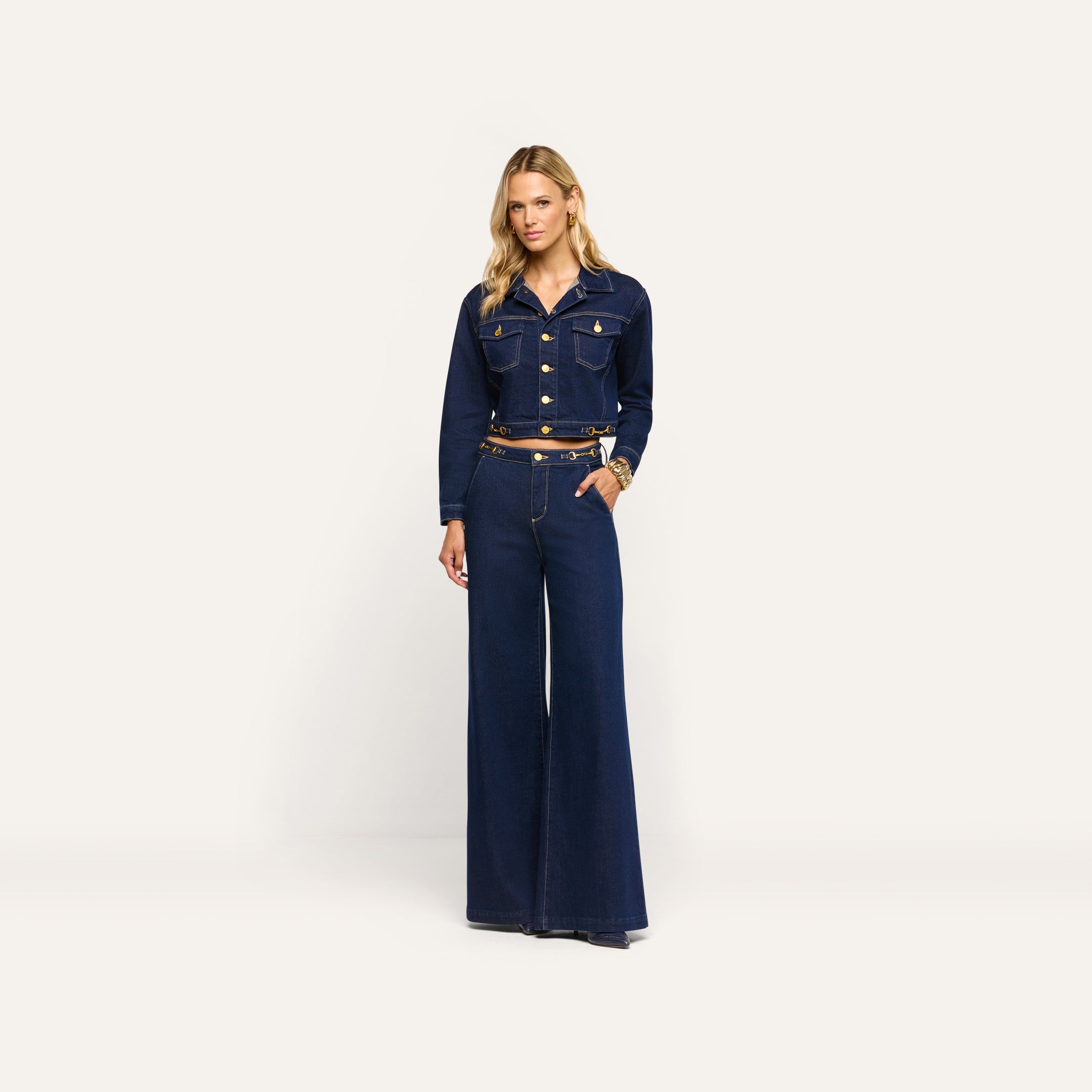 A model wearing the Edin Jean Jacket in cropped indigo wash denim with gold buttons and matching high-waisted wide-leg jeans.