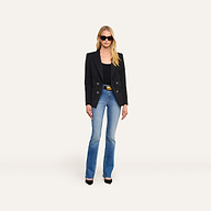 A woman stands against a plain white background, facing forward with her hands at her sides, wearing sunglasses, the Kiora Blazer—tailored with an hourglass silhouette—in black, paired with a black top, blue jeans, and black heels.