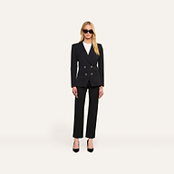 A woman stands facing forward against a plain white background, wearing the Kiora Blazer—a black double-breasted blazer with a tailored hourglass shape—paired with a white top, black heels, and sunglasses.
