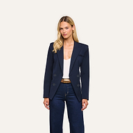 A woman stands facing forward against a plain light background, wearing the Kiora Blazer in navy, styled with a white top and dark blue jeans.