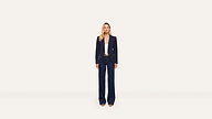 A woman stands facing forward, wearing a navy blazer, wide-leg navy pants, a white top, and tan heels against a plain white background. The tailored blazer adds a polished touch to her ensemble.