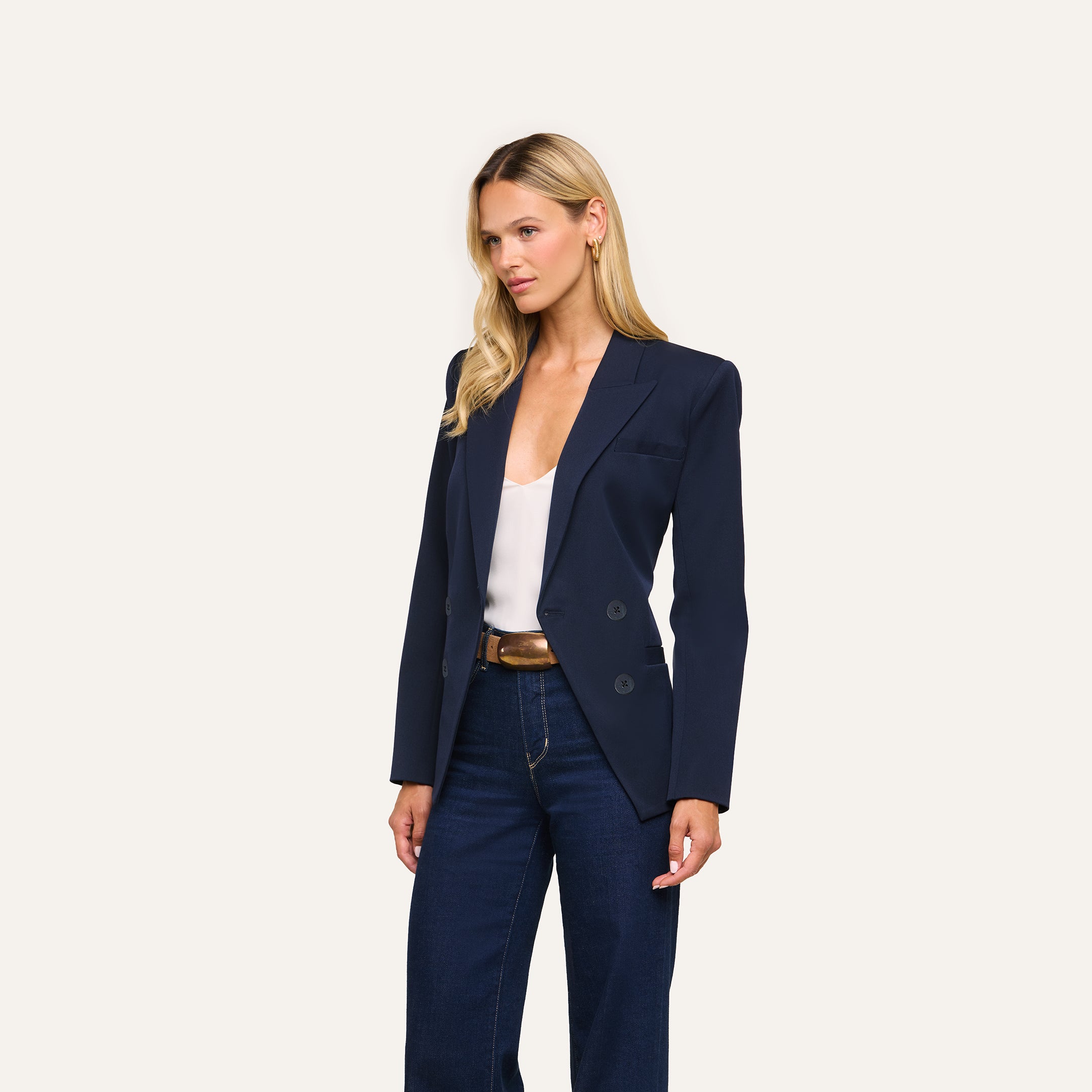 A woman with long blonde hair models the Kiora Blazer in navy over a white top and dark jeans, posing against a plain light background.