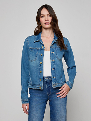 A woman with long, brown hair wears a slim fit Celine Jean Jacket over a white top and blue jeans, standing against a plain light gray background.