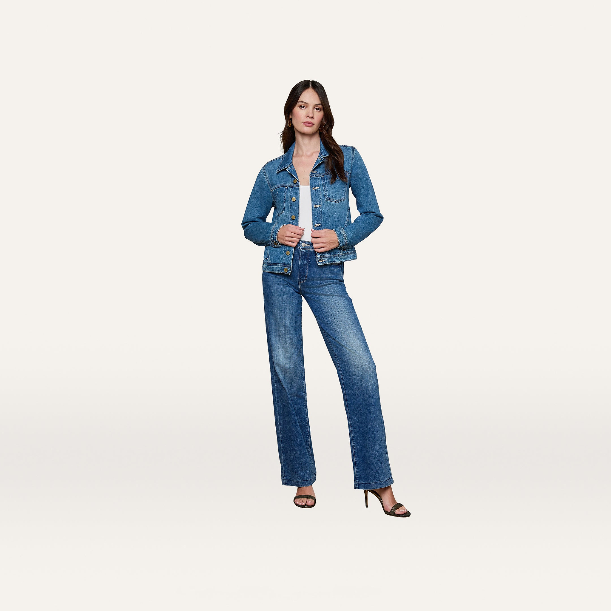 The woman stands in a slim fit, featherweight L’AGENCE Celine Jean Jacket and matching jeans with black high heels against a plain white background.