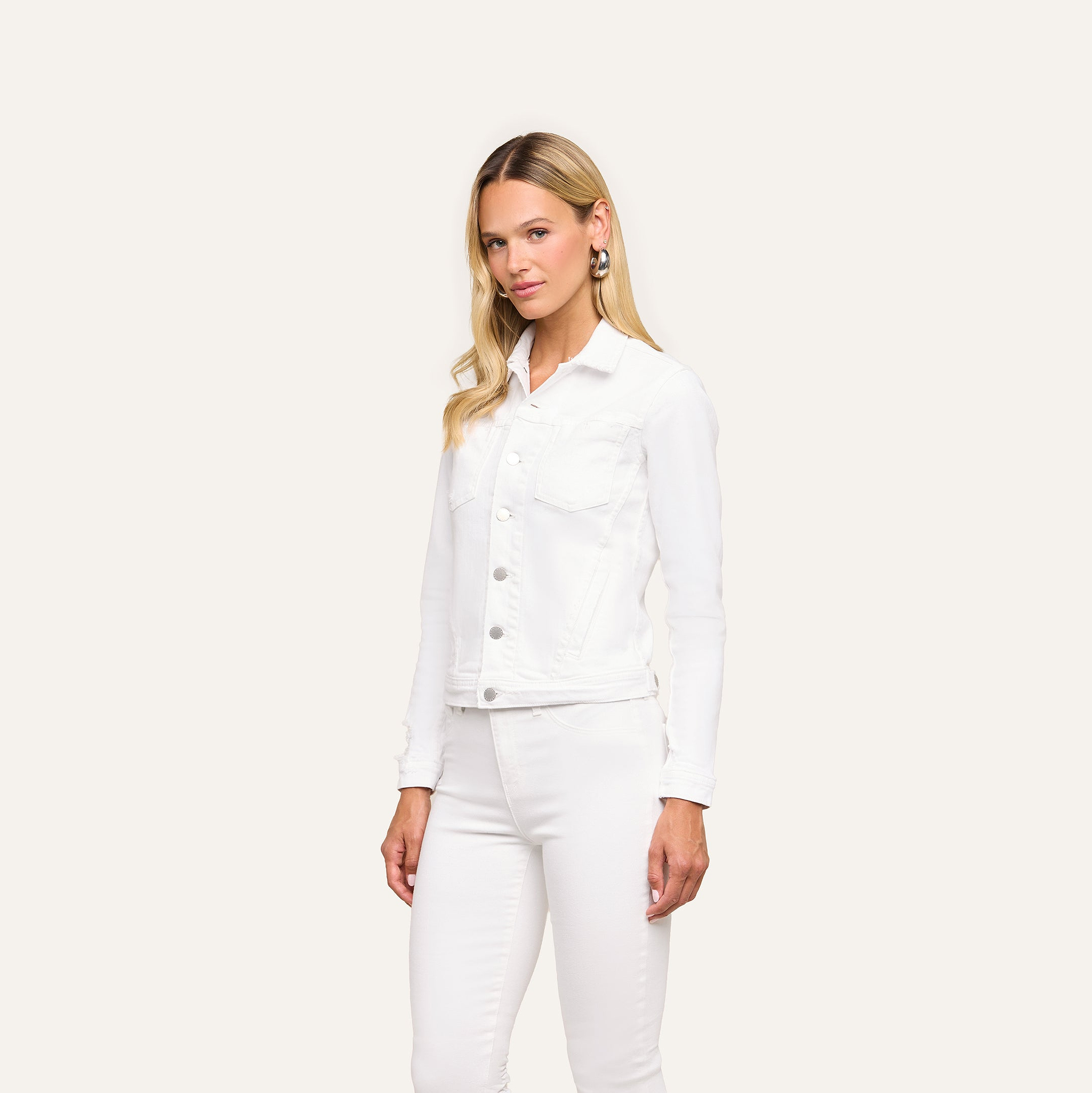 A woman with long blonde hair wears the Celine Jean Jacket and optic white pants, standing against a plain light background with a neutral expression and arms by her sides.