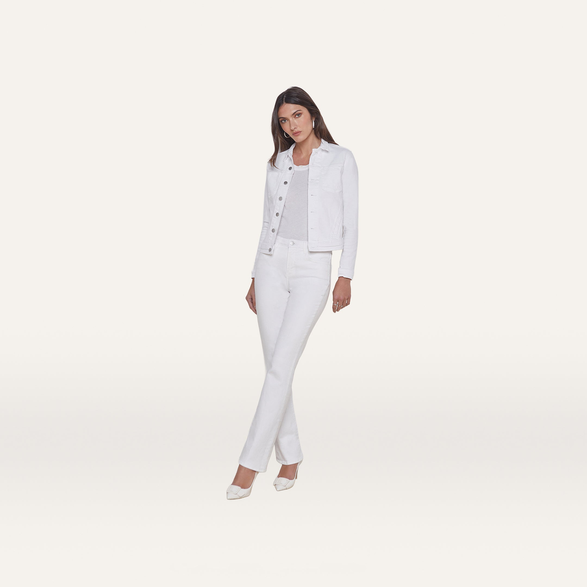 A woman stands facing forward, wearing the Celine Jean Jacket in optic white with a relaxed fit, paired with white pants, a light top, and white shoes against a plain white background.