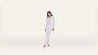Woman standing and posing in all-white clothing: a denim jacket, top, jeans, and heels, against a plain white background.