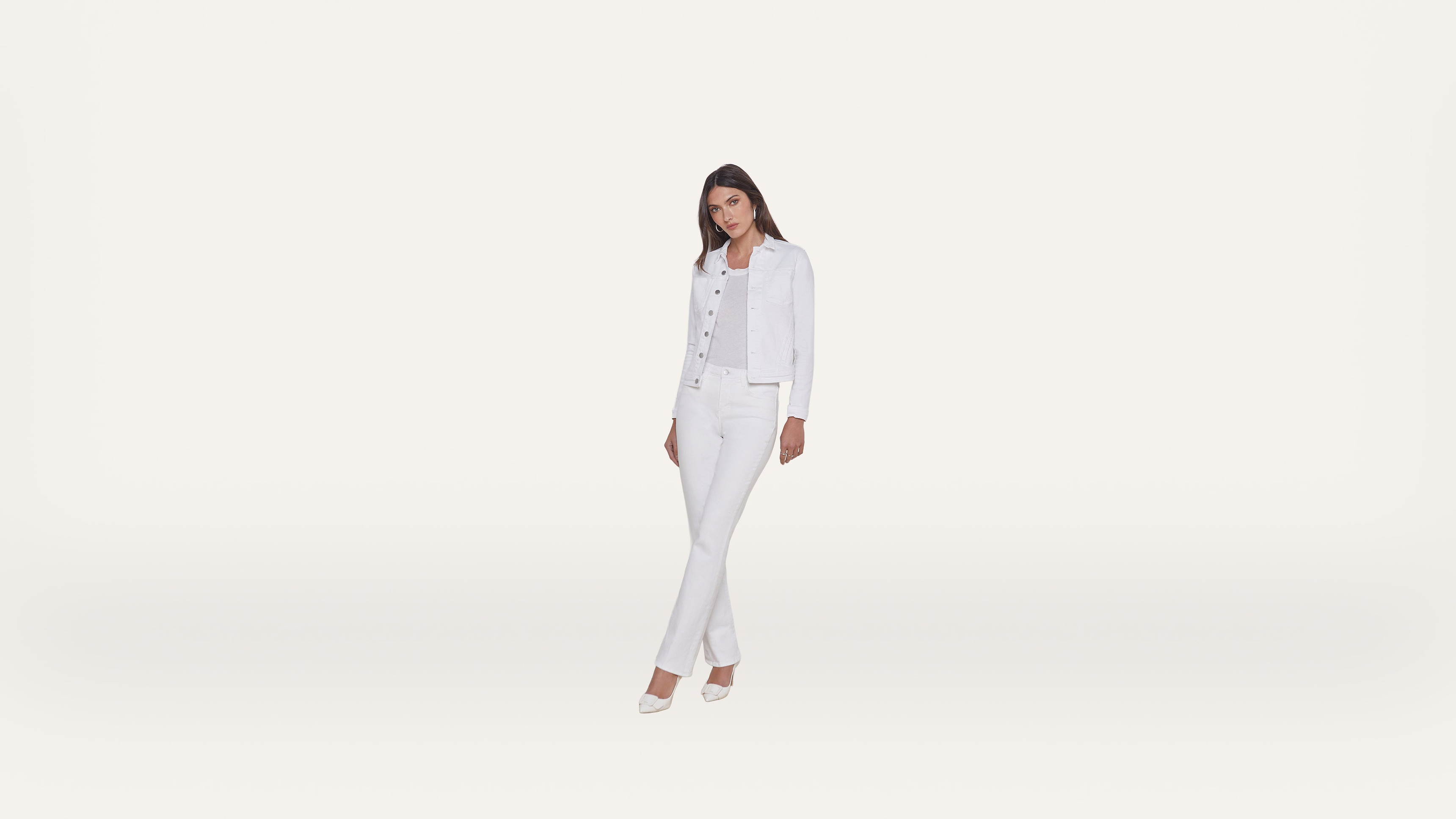 Woman standing and posing in all-white clothing: a denim jacket, top, jeans, and heels, against a plain white background.