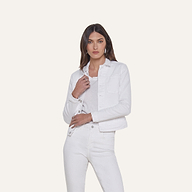 A woman stands against a plain background, wearing the Celine Jean Jacket in optic white with a relaxed fit, layered over a matching shirt and white jeans. She has straight brown hair and a neutral expression, with one hand touching the jacket near the collar.