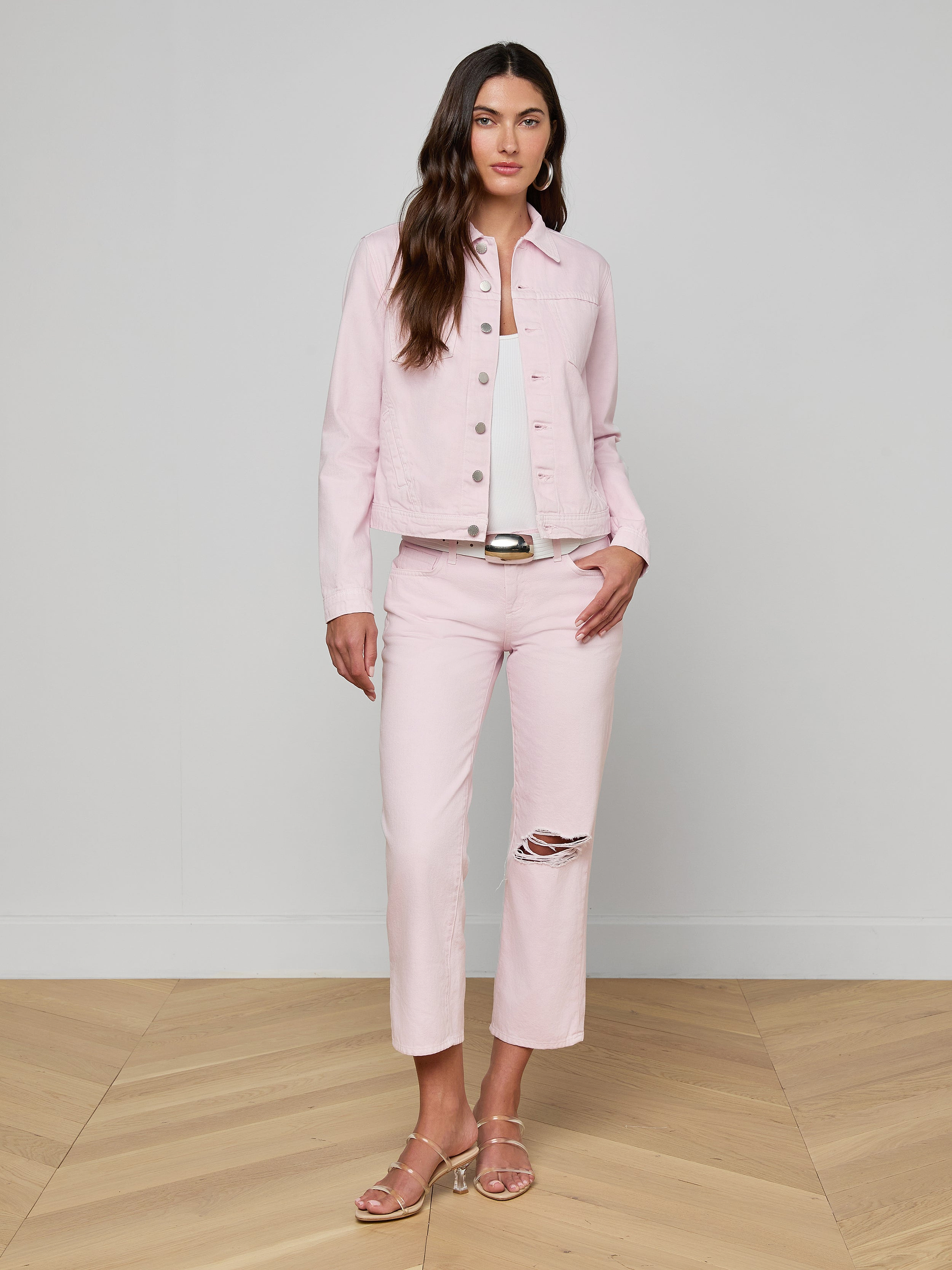 A woman stands against a white background wearing a pastel lilac Celine Jean Jacket in a slim fit, paired with matching pants featuring a rip at the knee and sandals.