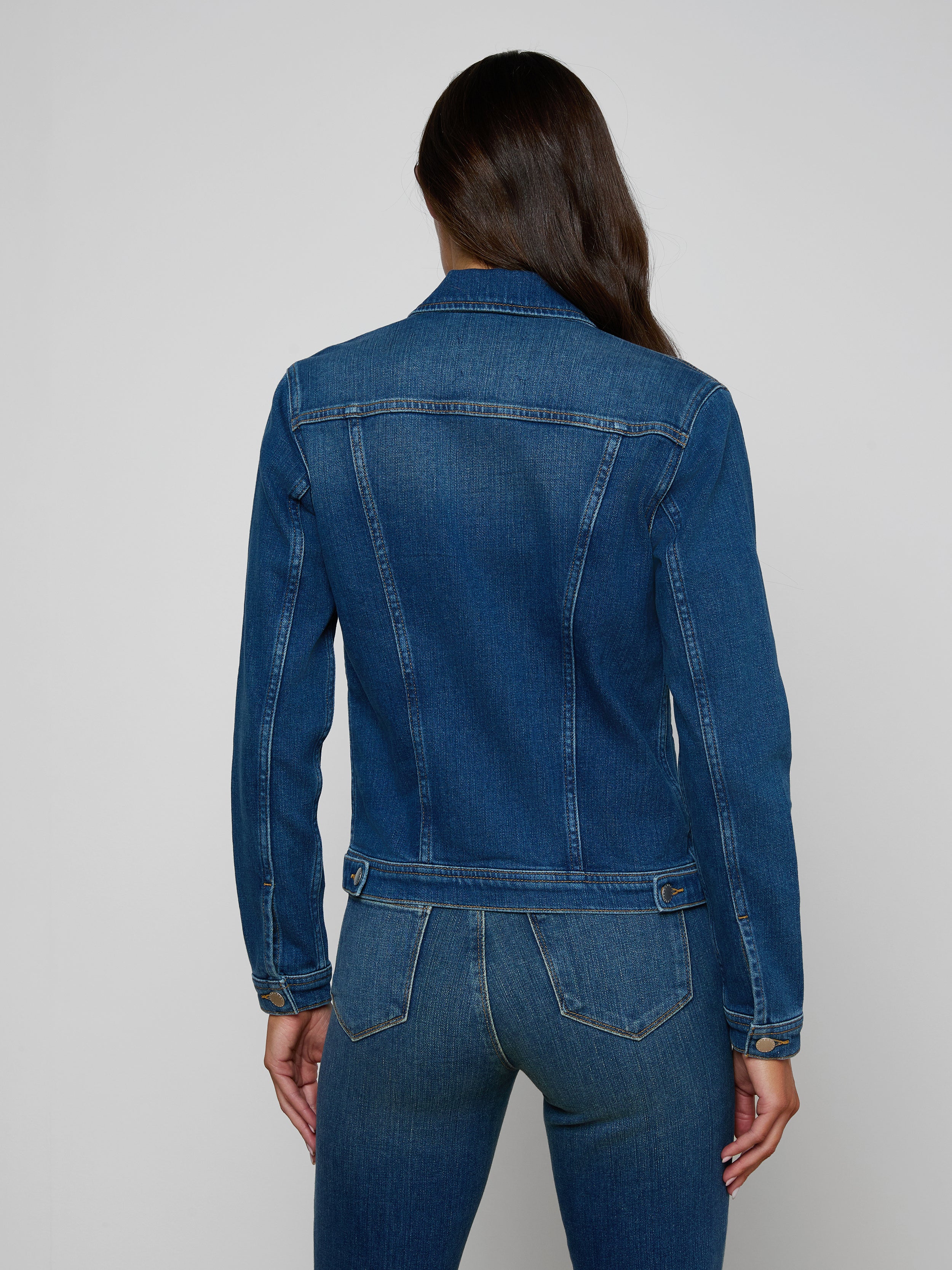 Woman with long brown hair wearing a vintage wash Celine Jean Jacket and slim fit jeans, facing away from the camera against a plain, light background.