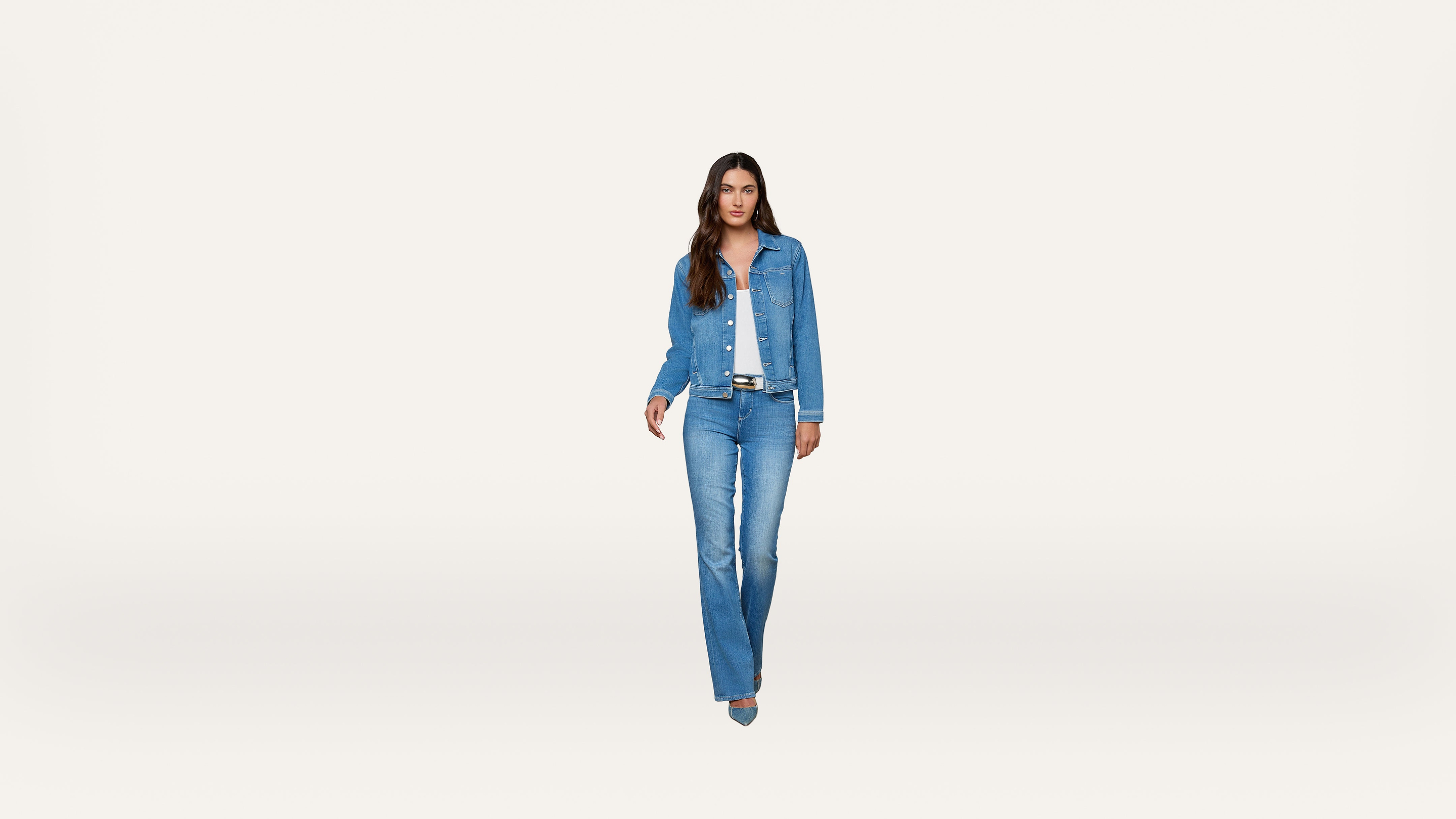 A woman stands facing forward, wearing a blue denim jacket, blue jeans, a white shirt, and blue shoes, against a plain white background.