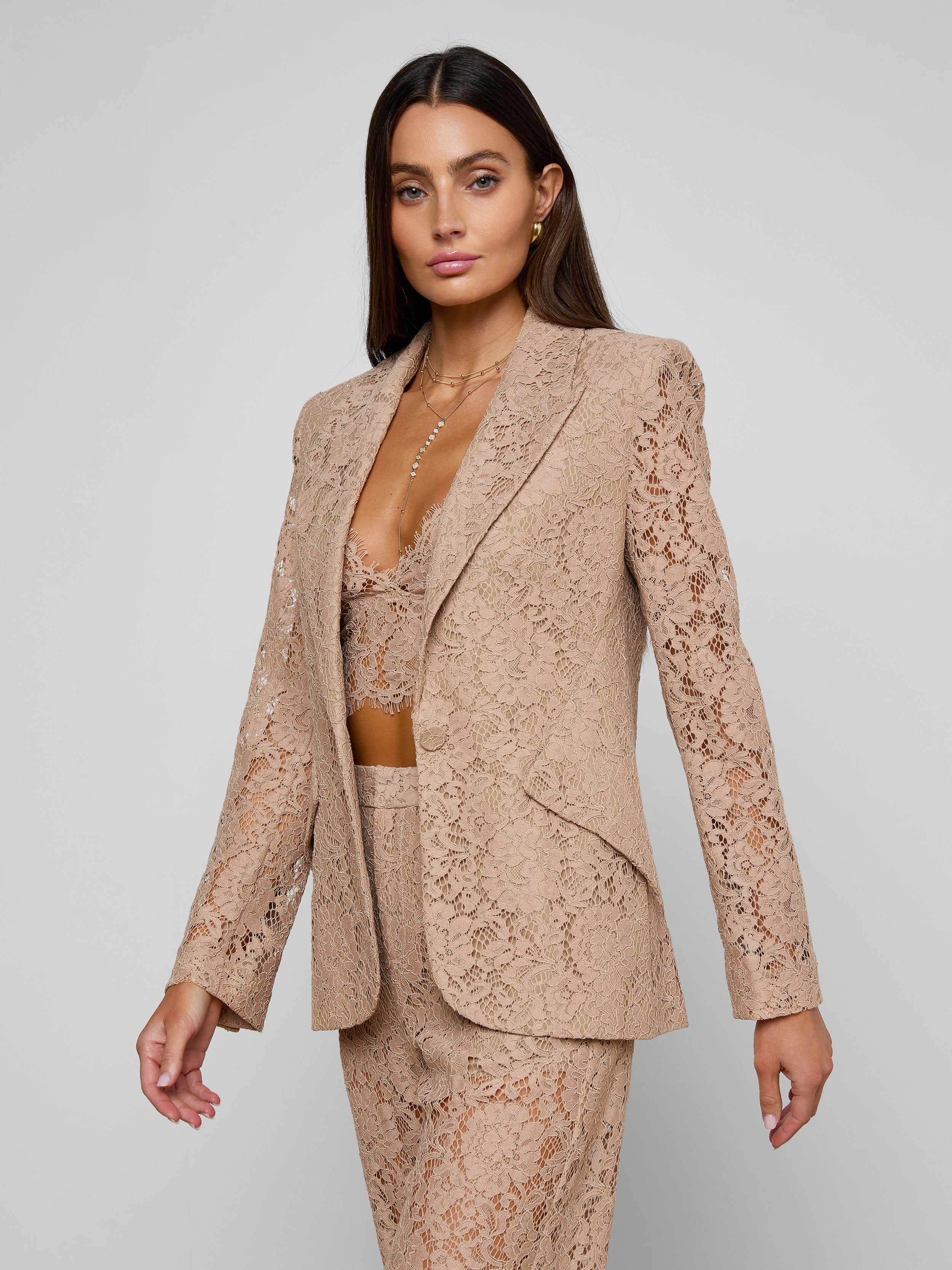 A woman wears the Chamberlain Lace Blazer with a matching bralette and pants, standing against a plain light background. This classic suit is perfect for an office-ready style.