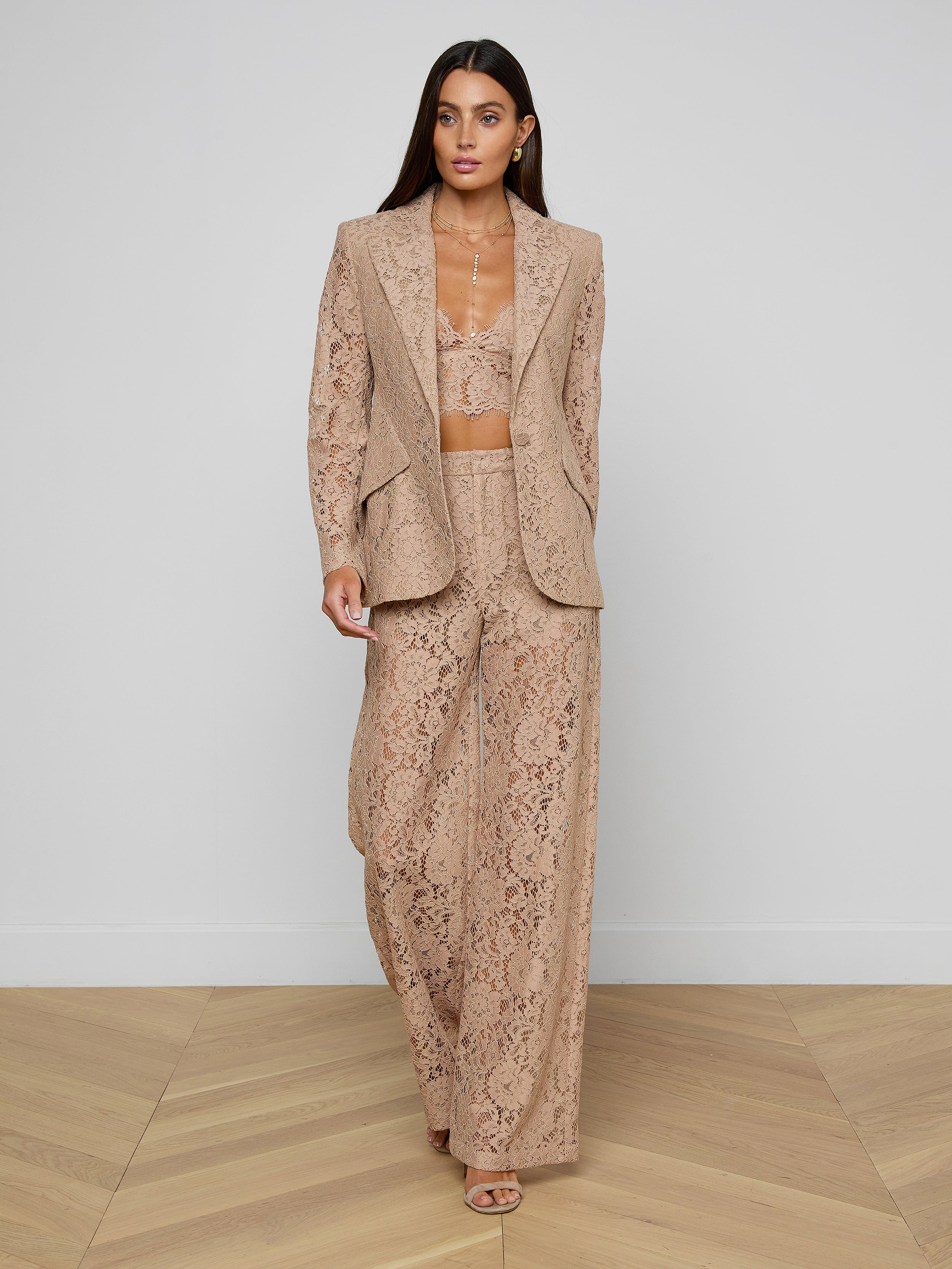 A woman walks forward wearing the Chamberlain Lace Blazer in tan floral lace, paired with wide-leg pants and a matching bralette, creating an office-ready style against a plain white background.