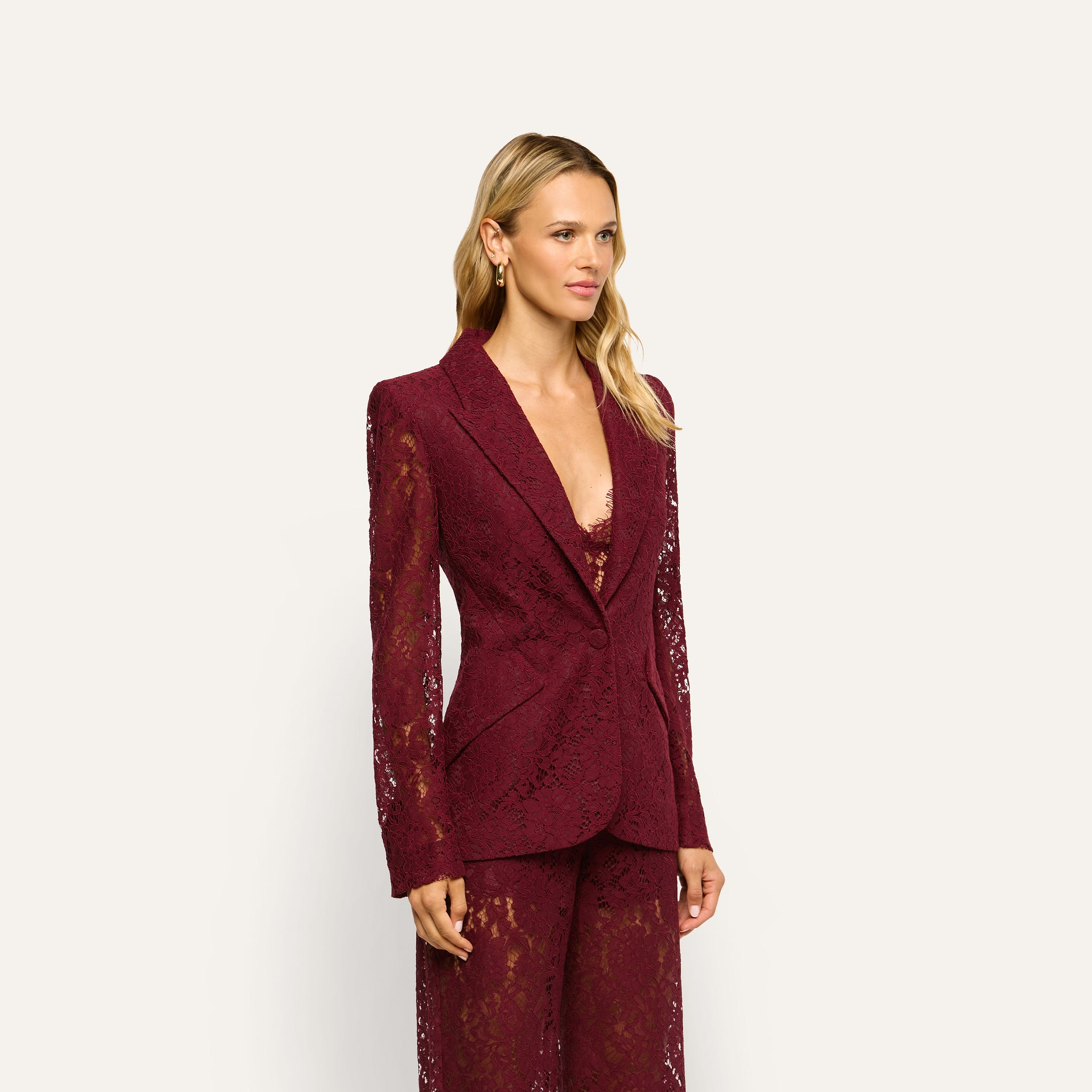 A person wears the Chamberlain Lace Blazer, a classic, long-sleeved, single-button jacket crafted from deep port red lace.