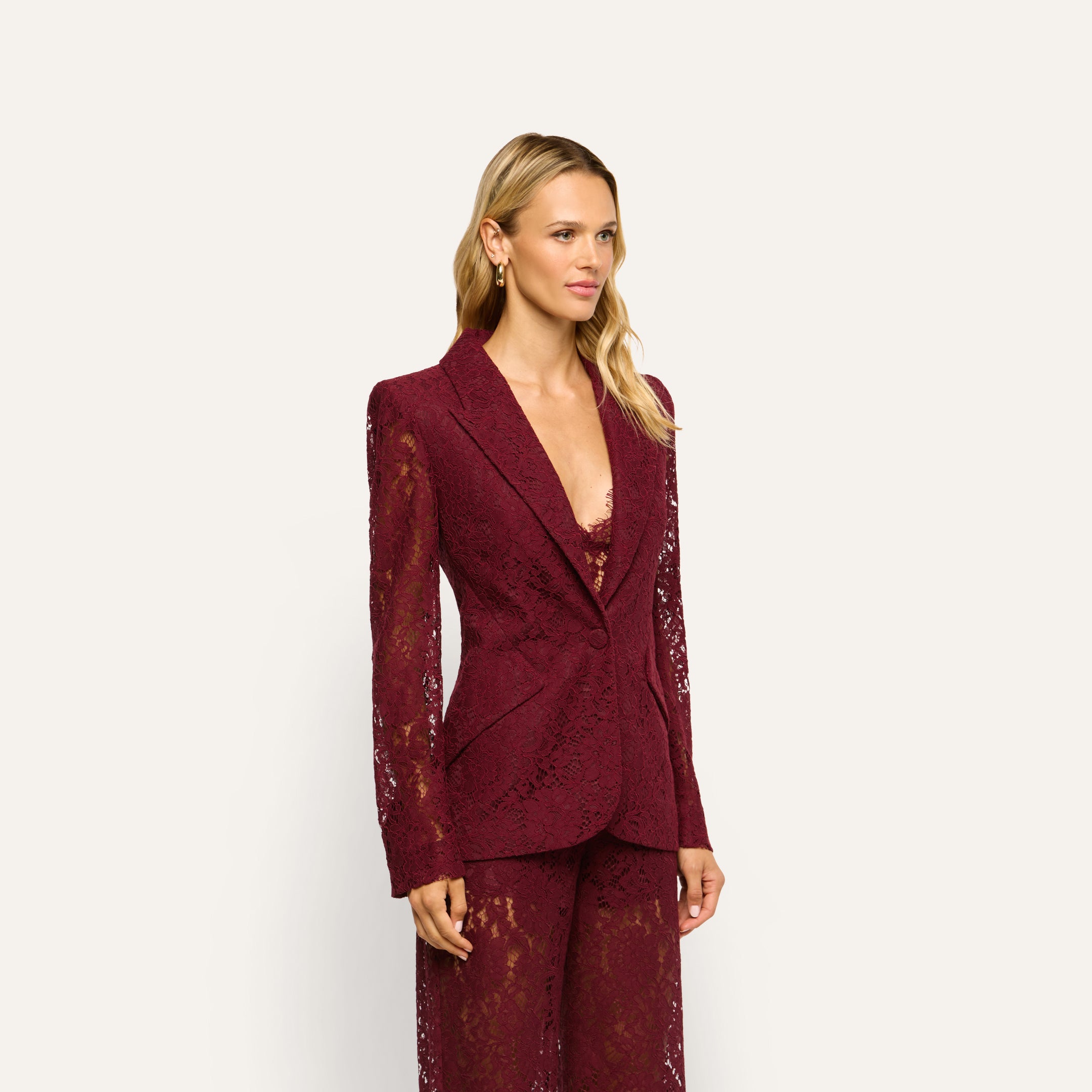 A person wears the Chamberlain Lace Blazer, a classic, long-sleeved, single-button jacket crafted from deep port red lace.