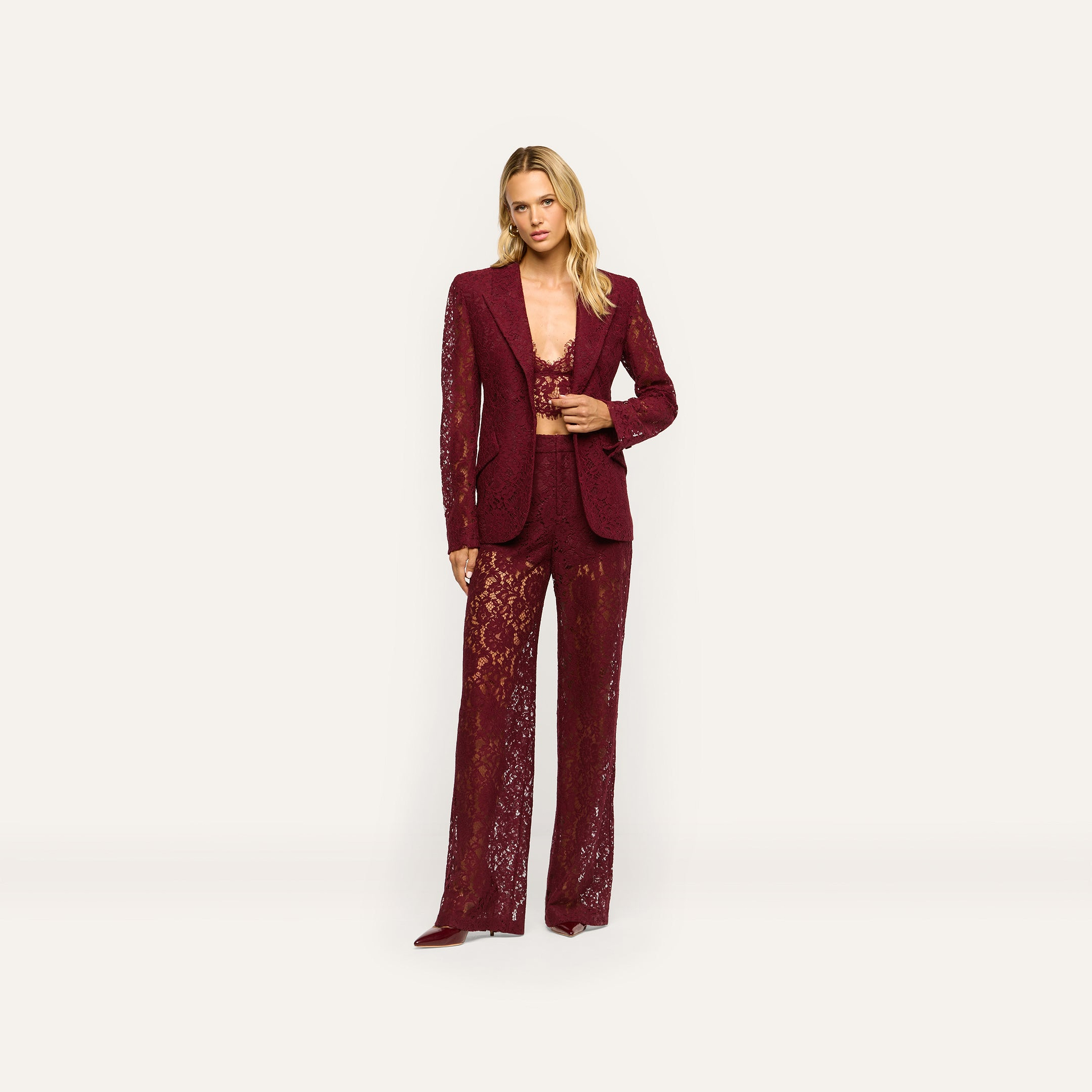 A woman wears a deep port red Chamberlain Lace Blazer with a matching cropped lace top and wide-leg lace trousers in a classic design.
