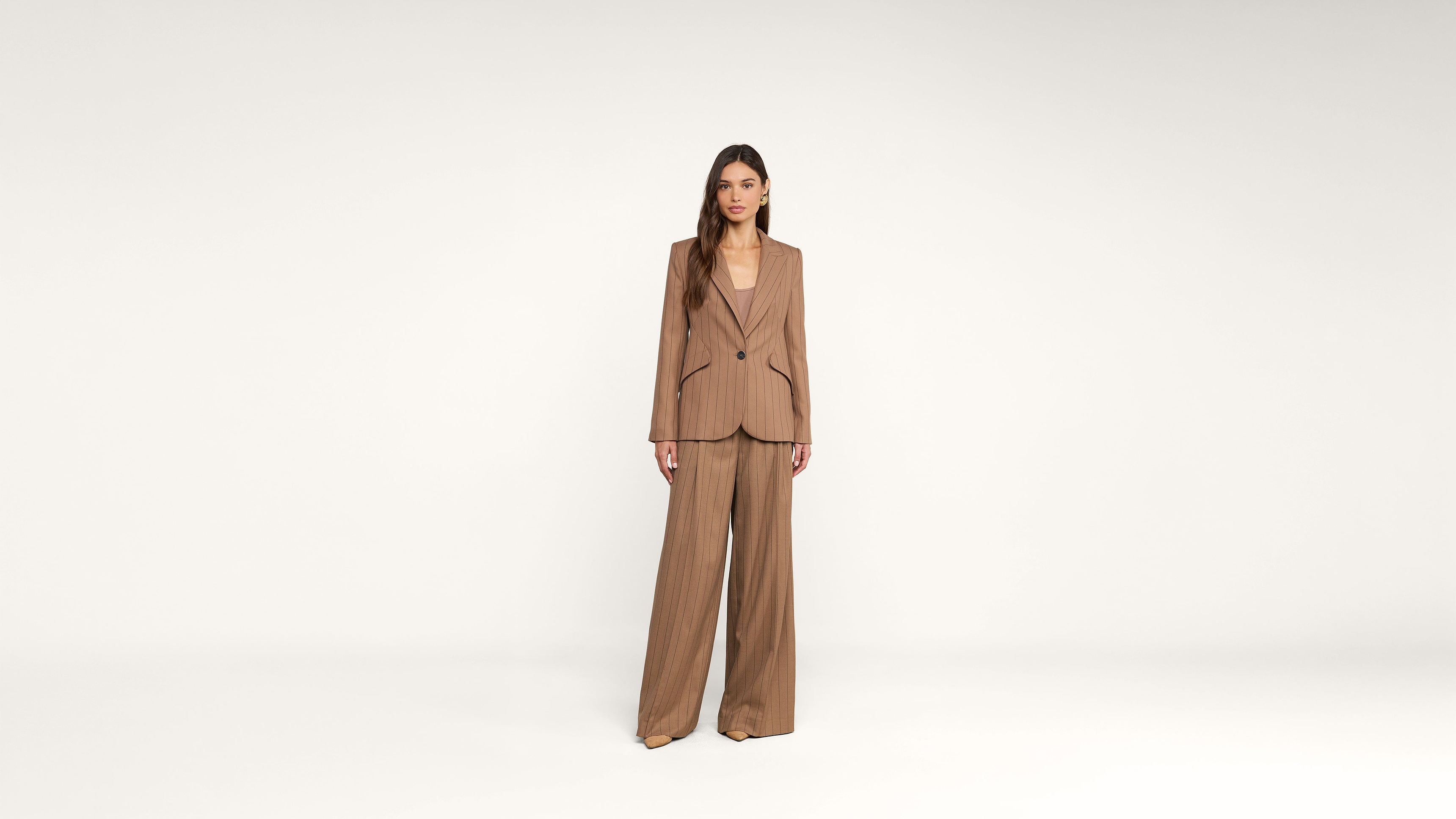 Woman standing facing forward, wearing a brown oversized blazer and matching wide-leg trousers, against a plain white background.