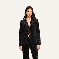 A woman with long dark hair wears the Chamberlain Velvet Blazer by L’AGENCE over a lacy top, standing against a plain light background.