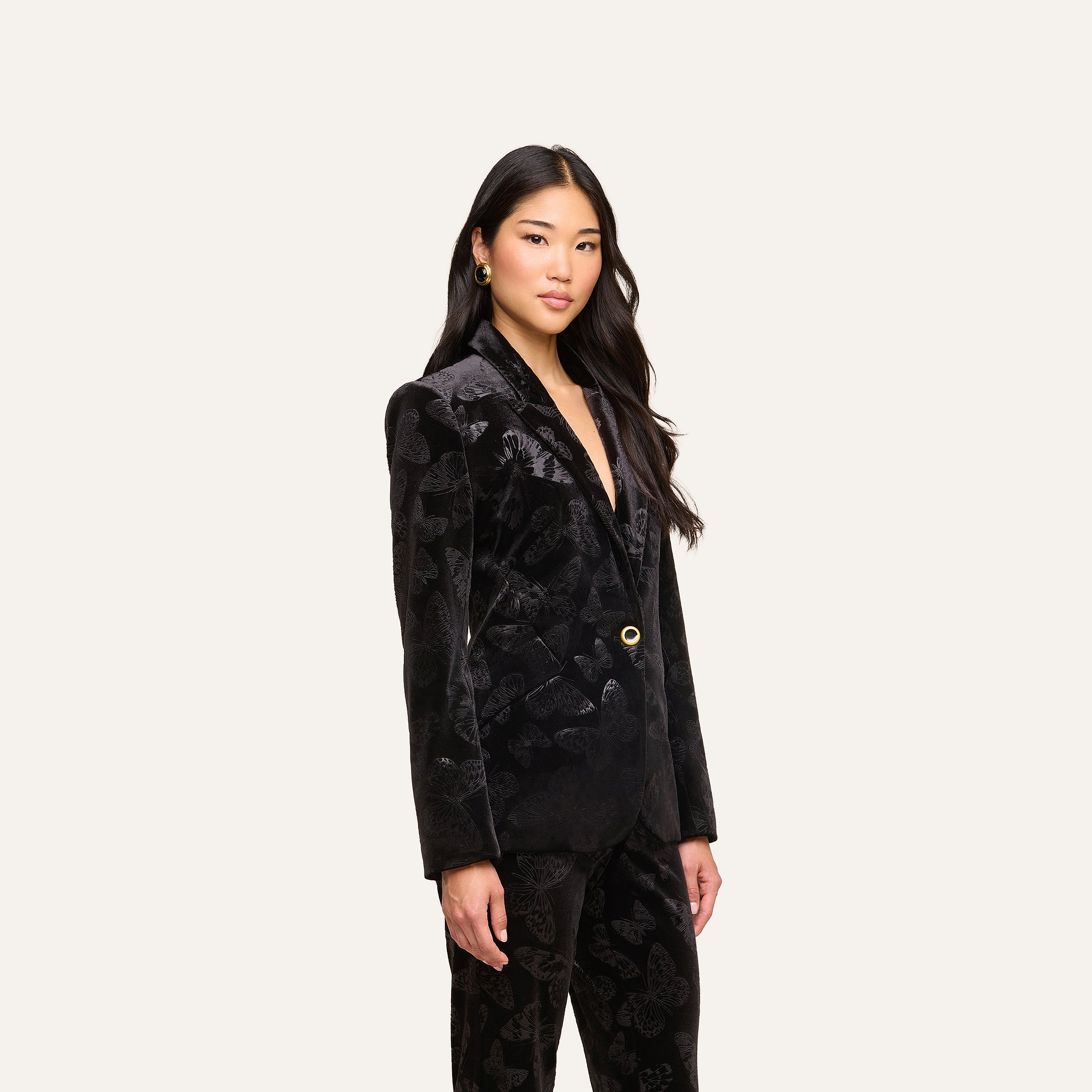 A woman with long dark hair wears the Chamberlain Velvet Blazer with matching pants, standing against a plain light background and looking confidently at the camera.