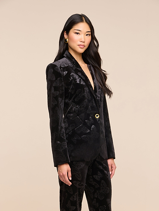 A woman with long black hair wearing a Chamberlain Velvet Blazer stands against a plain beige background, looking at the camera with a neutral expression.