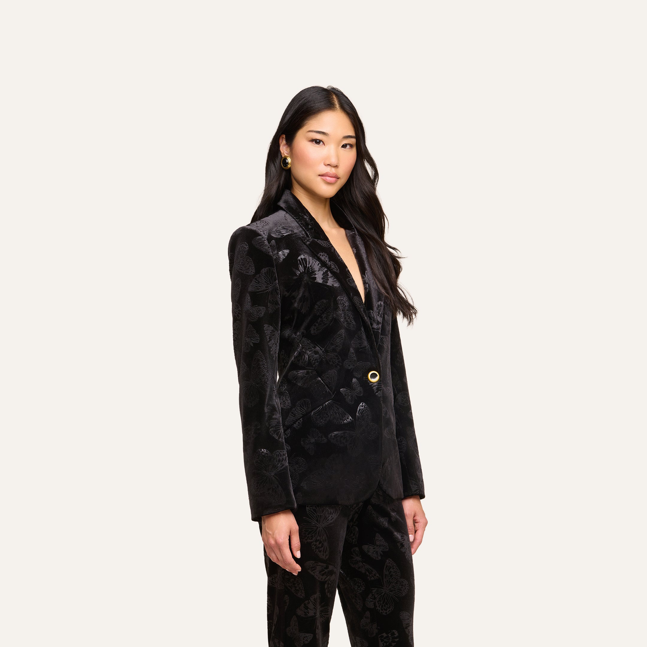 A woman with long dark hair wears the Chamberlain Velvet Blazer with matching pants, standing against a plain light background and looking confidently at the camera.