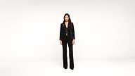 A woman stands facing forward in a black velvet suit and heels against a plain white background.