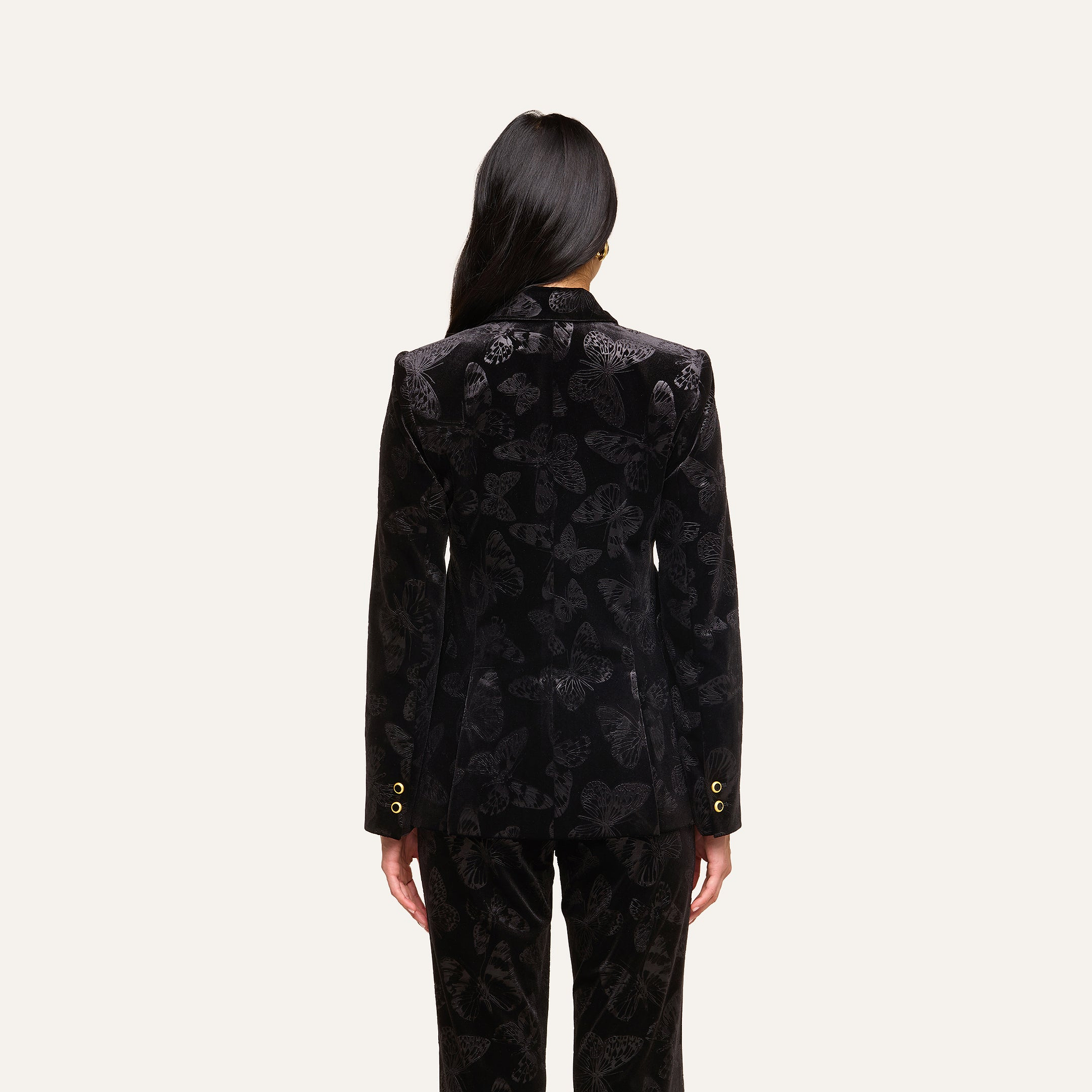 A person with long dark hair, wearing the Chamberlain Velvet Blazer from L’AGENCE, is standing and facing away from the camera against a plain light background.