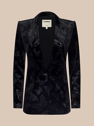 The Chamberlain Velvet Blazer features a black butterfly-embossed velvet design with notched lapels and a single button closure, showcased against a beige background. Drawing inspiration from the L’AGENCE Chamberlain silhouette, this blazer embodies effortless sophistication.