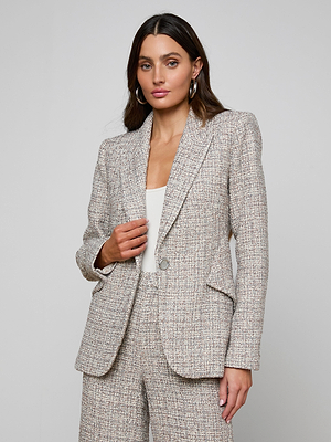 A woman with long brown hair wears the Chamberlain Tweed Blazer and matching trousers in dusty blue over a white top, standing against a light gray background and looking at the camera with a neutral expression.