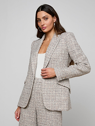Wearing the Chamberlain Tweed Blazer with matching trousers and a white top underneath, a woman with long dark hair and hoop earrings poses against a plain, light background.