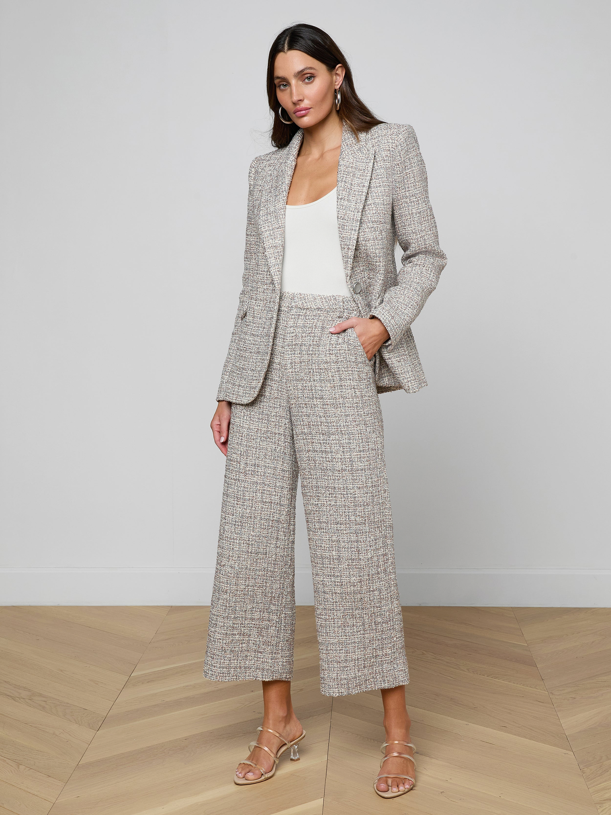 A woman stands against a plain light background wearing the Chamberlain Tweed Blazer in gray plaid, paired with matching wide-leg cropped pants, a white top, and beige heeled sandals.