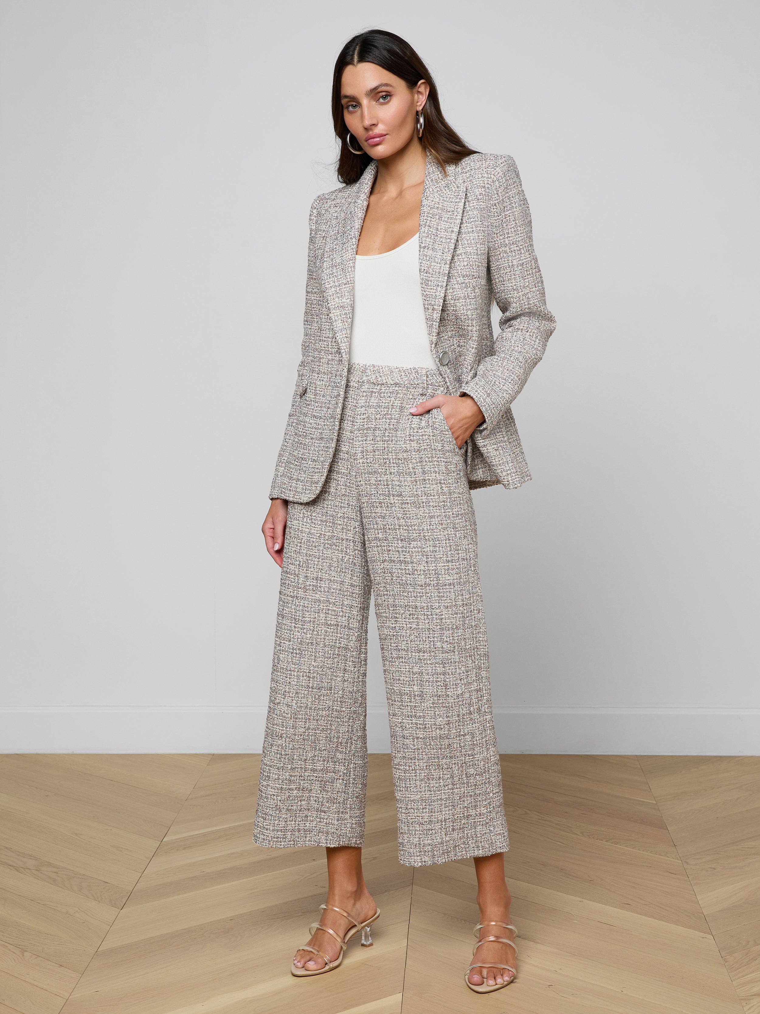 A woman stands against a plain light background wearing the Chamberlain Tweed Blazer in gray plaid, paired with matching wide-leg cropped pants, a white top, and beige heeled sandals.