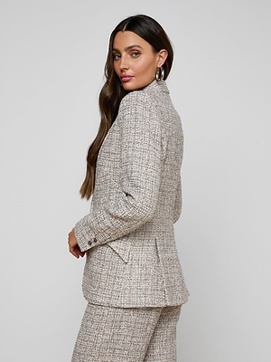 A woman with long brown hair wears the Chamberlain Tweed Blazer in dusty blue and large hoop earrings, standing sideways and looking over her shoulder against a plain light background.
