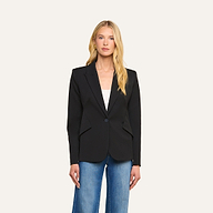 A woman with long blonde hair wears the Chamberlain Blazer, a black single-breasted jacket crafted with precision tailoring, layered over a white top and blue jeans, standing against a plain light background.