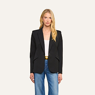 A woman with long blonde hair, wearing the Chamberlain Blazer—crafted from black twill suiting in a single-breasted silhouette—over a white top and blue jeans, stands facing forward against a plain light background.